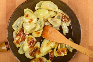 Tepeden çekimde açık yeşil çan biberi dilimleri koyu bir tavada kahverengileşirken ahşap bir spatulayla ahşap bir yüzey üzerinde durmaktadır.