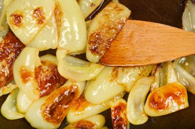 Tahta bir spatula, açık yeşil çan biberi dilimlerini karıştırır. Koyu bir tavada kahverengileşir. Bu da pişirildiklerini gösterir.