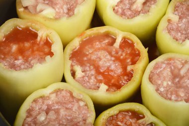 Yakın plan, tepeden çekimde et ve pirinç karışımı ile doldurulmuş çiğ yeşil çan biberleri görülüyor, bazıları canlı kırmızı domates sosuyla kaplanmış, pişirmeye hazır.