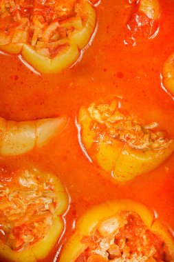 Yakın plan çekimde et ve pirinç karışımı ile doldurulmuş açık yeşil dolma biberler bol, kaynayan portakal kırmızısı domates sosuna batırılmıştır.