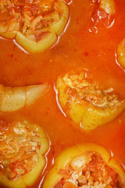 Yakın plan çekimde et ve pirinç karışımı ile doldurulmuş açık yeşil dolma biberler bol, kaynayan portakal kırmızısı domates sosuna batırılmıştır.