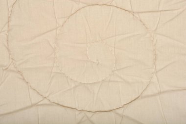 Sarmal dikiş desenli bej bir yorganın yakın plan çekimi.