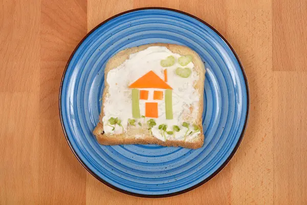 Tepeden tırnağa krem peynirli bir dilim ekmekle yapılan eğlenceli ve yenilebilir bir ev yapımı. Mavi tabakta servis ediliyor.