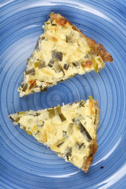  İki üçgen peynirli ve pırasalı kiş mavi seramik tabakta sunuluyor.