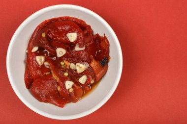 Beyaz bir kase parlak kırmızı biber ve sarımsak dilimleriyle dolu, canlı kırmızı arka planda geniş bir kopya alanı var.