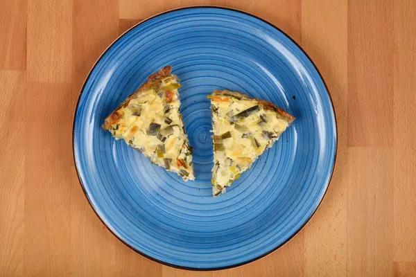  İki üçgen peynirli ve pırasalı kiş ahşap bir yüzeyde mavi bir seramik tabakta sunuluyor..