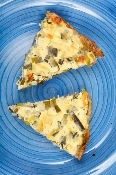  İki üçgen peynirli ve pırasalı kiş mavi seramik tabakta sunuluyor.