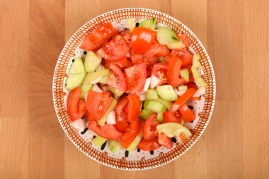 Tahta zemin üzerinde bir kase taze doğranmış domates, salatalık, dolma biber ve soğan salatası, tepeden tırnağa çekilmiş.