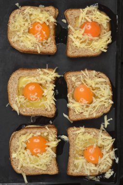 Altı parça kızarmış ekmek, içi çiğ yumurta ve rendelenmiş peynirle dolu, koyu bir yemek tepsisi üzerine dizilmiş.