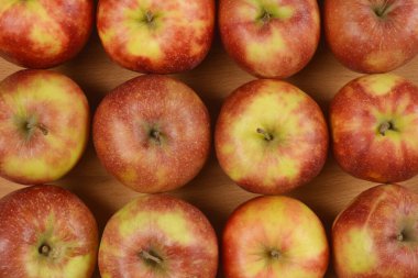 Ahşap bir yüzey üzerinde düzgün sıralanmış kırmızı ve yeşil elmalardan oluşan bir ızgaranın genel görünümü