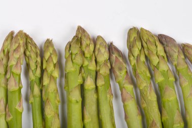 Yakın plan, birkaç taze yeşil kuşkonmaz mızrağının ucunu düz beyaz arka planda gösterir.