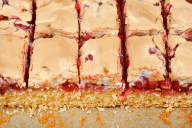 Yakın plan, göz hizasında bir fotoğraf üzümlü üzümlü ve kremalı kekin taze karelerini gözler önüne seriyor, altın sünger keki farklı katmanlarını seriyor, canlı kırmızı meyve dolgusu, ve fırında pişmiş kremanın tepesini..