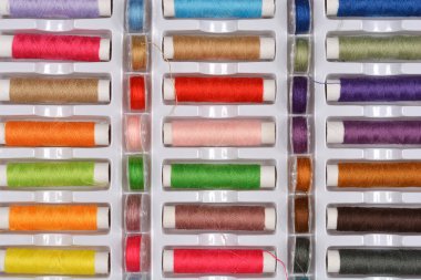 Beyaz plastik bir kutuya düzgünce yerleştirilmiş renkli dikiş ipliklerinden oluşan geniş bir çeşitliliğin yukarıdan aşağı görüntüsü.