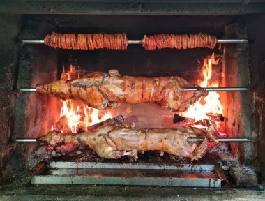 Büyük ahşap kaplı bir fırında koca bir emziren domuz ve ateşte kızaran bir kuzu bulunur. Üzerlerinde domuz eti de vardır.