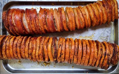 İki uzun rulo domuz eti, kalın kesikler halinde dilimlenmiş, servis için hazır metal bir tepside yatıyor.