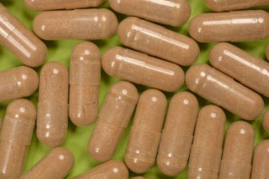 Açık yeşil arkaplandaki dağınık bej kapsüllerin yakın plan görüntüsü.