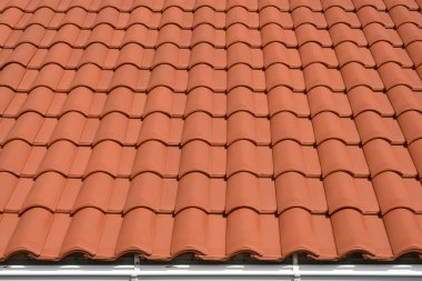 Terracotta çatı kiremitlerinin canlı ve tekdüze deseni çerçeveye yayılarak klasik kıvrımlı şekillerini ve altta beyaz bir oluktan görünen kırmızımsı-kahverengi tonlarını gözler önüne seriyor.