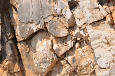 Yakın plan çekimde bir kaya yüzeyinin karmaşık ve engebeli dokusu ortaya çıkar. Gri ve bej tonlarında derin çatlaklar ve gölgelerle karakterize edilir.