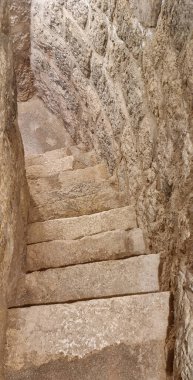 Taş basamaklar sönük, kadim görünümlü, pürüzlü duvarlı bir geçide iniyor.