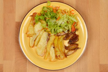 Sarı tabakta bol bol kızarmış patates, doldurulmuş mürekkep balığı ve ahşap bir masada taze yeşil salata bulunur.