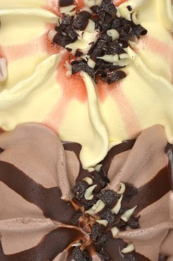 Yakın plan dikey çekimde, üzerinde koyu ve beyaz çikolata parçacıkları bulunan vanilyalı ve çikolatalı dondurma aromaları gösterilir.