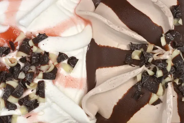 Yakından bakınca stracciatella ve fındıklı dondurma aromalarının kıvrımlı dokularının koyu ve beyaz çikolata parçacıklarıyla kaplı olduğunu görüyoruz.