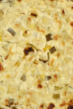  Yakın çekim, yukarıdan aşağıya doğru bir manzara ev yapımı peynir ve pırasa kekinin altın-kahverengi kabuğunu ve kremasını ön plana çıkarıyor.