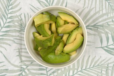 Avokado dilimlenmiş bir kase palmiye yaprağı desenli masa örtüsü.