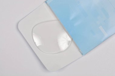 Tek bir temiz gözlük merceği kısmen görülebilir mavi ve beyaz kağıt paketleme, düz bir arkaplan karşı ayarlanır