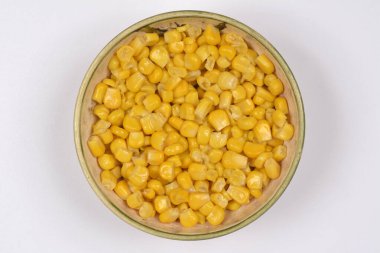 Bir tepeden çekimde parlak, sarı mısır taneleriyle dolu kırsal seramik bir kase, temiz beyaz arka planda sunuluyor.