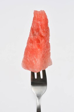 Tek, sulu bir dilim kırmızı karpuz, temiz ve açık bir arkaplan ile gümüş çatalın dişleri üzerinde mükemmel bir şekilde dengelenmiştir.