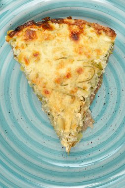 Detaylı, tepeden tırnağa, altın fırında pişmiş kabak ve pırasalı kiş dilimini mavi bir seramik tabakta dinlenirken gösteriyor.