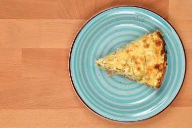 Lezzetli bir parça kabak ve pırasalı kiş açık renkli ahşap bir masa üzerinde geniş bir kopya alanı olan mavi bir seramik tabakta duruyor.