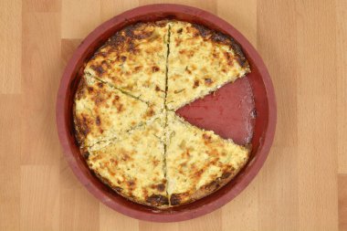 Lezzetli bir kabak ve pırasalı kiş, bir dilim kesilmiş, ahşap bir yüzey üzerinde yuvarlak kırmızı bir fırın kabında sunulur.