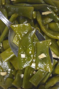 Yakından bakınca bir kaşık dolusu taze fasulye ve salatanın üzerine yerleştirilmiş sarımsaklı salata görünüyor.