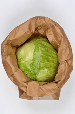 Bu kuş bakışı görüntü, buruşmuş kahverengi bir kesekağıdına yerleştirilmiş yeşil bir marul başlığını gösteriyor. Mutfak kullanımına hazır.