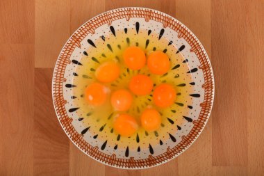 Tahta bir yüzey üzerinde beyaz ve sarı bir seramik kasede çiğ yumurtanın yüksek açılı, yakın plan görüntüsü.