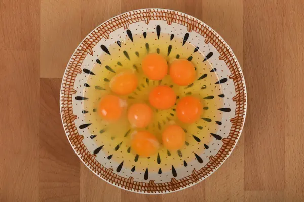 Tahta bir yüzey üzerinde beyaz ve sarı bir seramik kasede çiğ yumurtanın yüksek açılı, yakın plan görüntüsü.