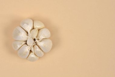 Yakın planda, merkezde, stüdyo çekimlerinde bej arka planda soyulmamış sarımsaklı karanfil kümesiyle sarımsak ampulü sergilenir.