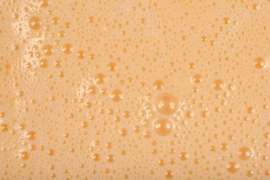 A full-frame, close-up shot captures the texture of a smooth, light beige liquid batter covered in tiny foam bubbles.