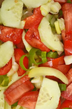 Detaylı bir yakın çekim, kırmızı domates kamaları, yeşil salatalık, biber dilimleri ve doğranmış taze soğan içeren taze kesilmiş salata sebzelerini gösteriyor.