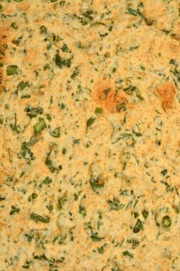 Pişmiş ev yapımı kraker yüzeyinin yakın plan bir görüntüsü. Kaba, açık kahverengi bir doku ve doğranmış yeşil maydanozu gösteriyor.