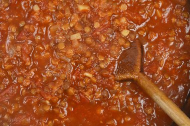 Ahşap bir kaşık tarafından karıştırılan bir tencere kalın, vejetaryen mercimek sosunun yakın çekim görüntüsü.