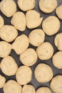 Yakın planda birçok ham hamur topunun siyah bir çarşaf üzerinde birbirine yakın sıralanmış bitkilerle benekli olduğu görülüyor.