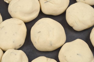 Yakın planda birçok ham hamur topunun siyah bir çarşaf üzerinde birbirine yakın sıralanmış bitkilerle benekli olduğu görülüyor.