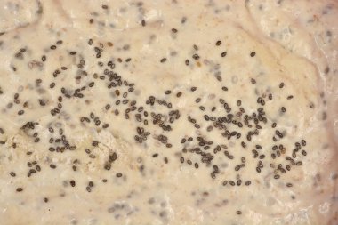 Bir makro yakın çekim çiğ ekmek hamuru yüzeyini yakalar cömertçe noktalanmış ve koyu chia tohumlarıyla kaplıdır.