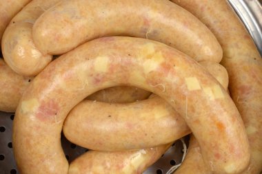 Yakın plan çekimde birkaç çiğ, ev yapımı tavuk sosisi ve metal buharlı tencereye kıvrılmış peynir parçaları var.