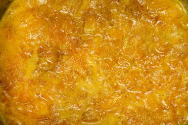 Yakından bakınca parlak turuncu mandalinalı marmelatların metal bir tencerede pişirildiğini ve doğranmış meyve parçalarını ön plana çıkardığını görüyoruz.