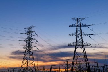 Elektrik iletim pilonu alacakaranlıkta mavi gökyüzüne karşı siluetlendi
