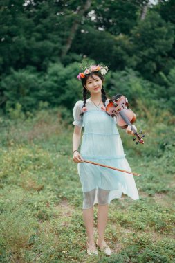 Kız büyük ağacın altında keman çalıyor.